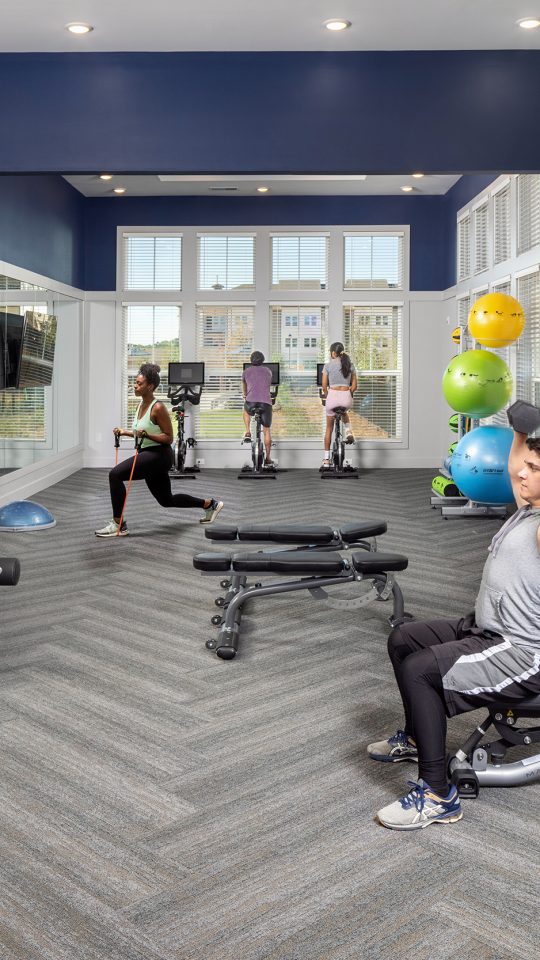 Four persons enjoying the indoor fitness center with weight machines and bikes