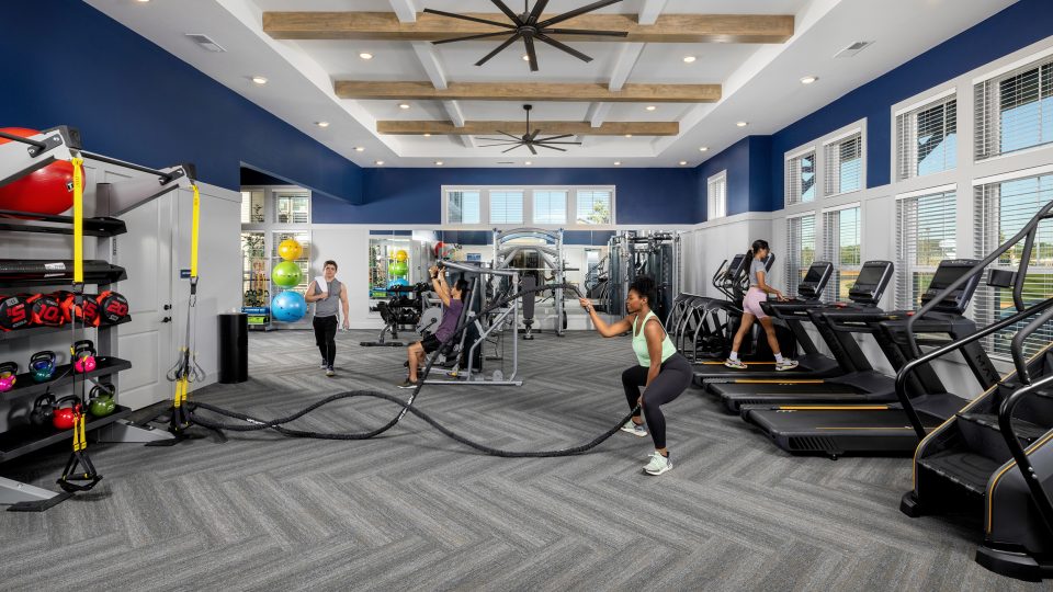 4 persons enjoying the indoor fitness center at Story Mundy Mill with treadmills, weight equipments, ropes, and large industrial ceiling fans